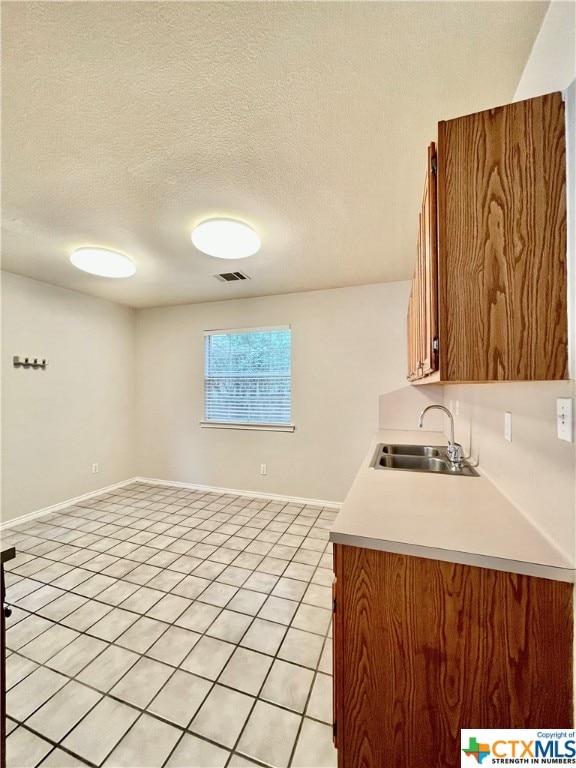 kitchen with a textured ceiling, sink, and light tile patterned flooring