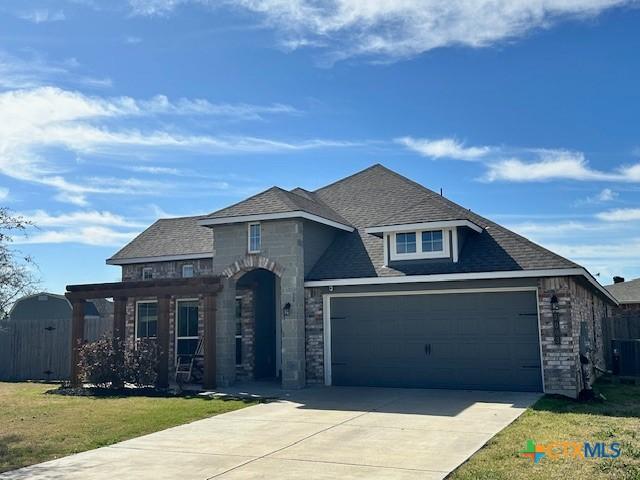 view of front of home featuring driveway, stone siding, an attached garage, fence, and a front yard