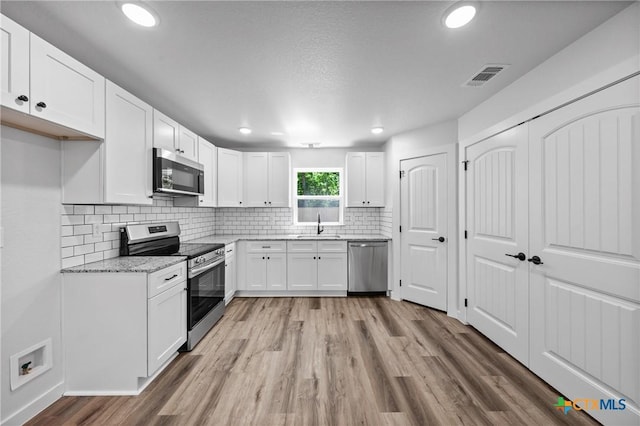 616 S 24th St, Temple, TX 76501 - kitchen featuring appliances with stainless steel finishes, light wood-style floors, white cabinets, a sink, and decorative backsplash