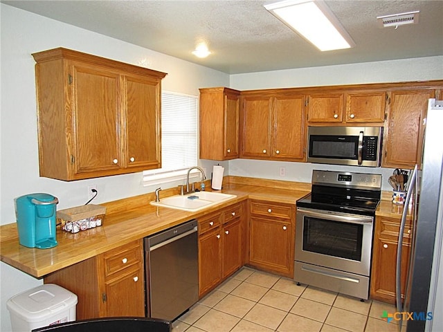 1104 N Blair St, Belton, TX 76513 - kitchen featuring stainless steel appliances, brown cabinets, light tile patterned flooring, and a textured ceiling