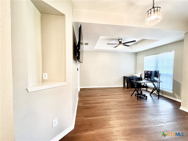 home office with ceiling fan with notable chandelier, wood-type flooring, and a raised ceiling