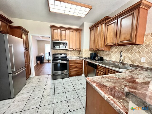 kitchen featuring light tile patterned flooring, backsplash, appliances with stainless steel finishes, sink, and dark stone countertops