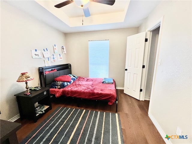 bedroom featuring dark hardwood / wood-style floors, ceiling fan, and a tray ceiling