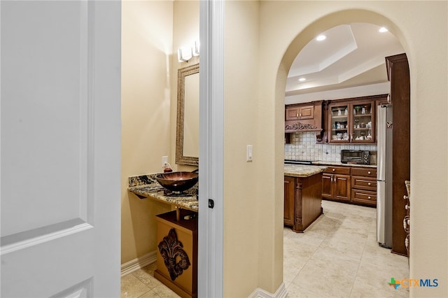 hall featuring sink, light tile patterned floors, and a raised ceiling