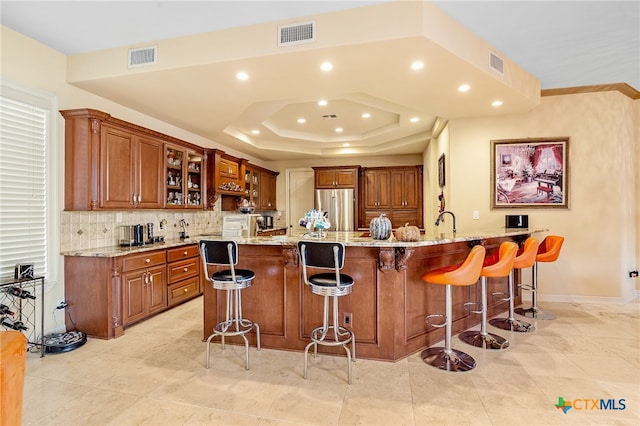 kitchen with a large island with sink, tasteful backsplash, light stone countertops, a breakfast bar area, and stainless steel fridge