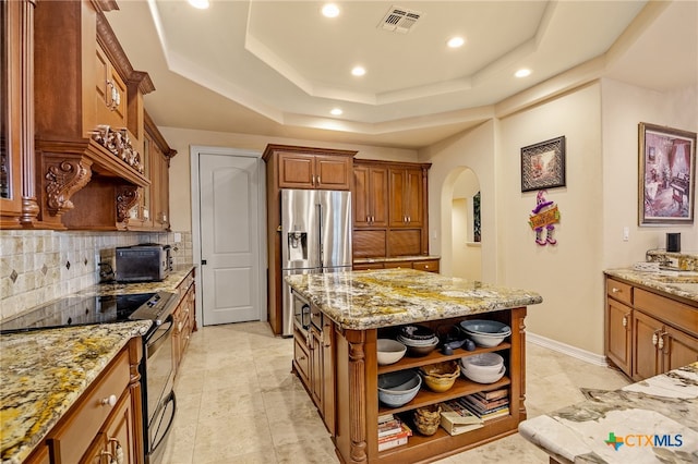 kitchen featuring appliances with stainless steel finishes, tasteful backsplash, light stone countertops, a tray ceiling, and a center island