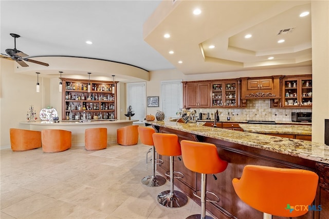 bar with tasteful backsplash, light stone countertops, pendant lighting, and ceiling fan