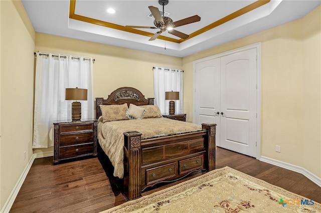 bedroom featuring a closet, dark hardwood / wood-style floors, a raised ceiling, and ceiling fan