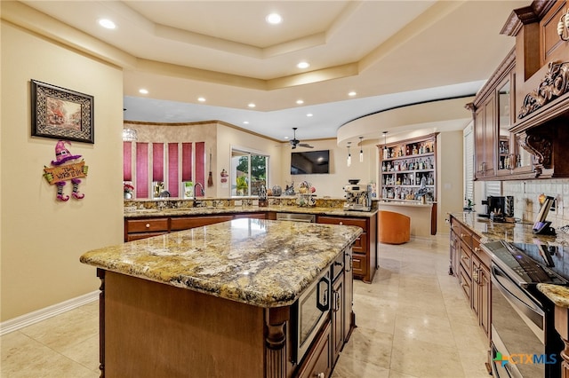 kitchen with light stone countertops, ceiling fan, decorative backsplash, and a kitchen island