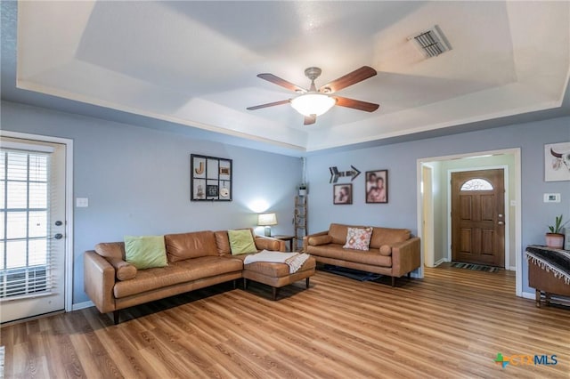 living room featuring a raised ceiling, ceiling fan, and light hardwood / wood-style flooring