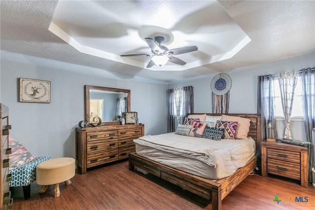 bedroom with dark hardwood / wood-style floors, ceiling fan, a tray ceiling, and a textured ceiling