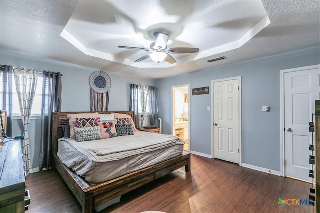 bedroom with dark hardwood / wood-style flooring, a tray ceiling, ensuite bath, and a textured ceiling