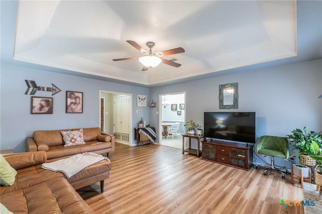 living room featuring a tray ceiling, light hardwood / wood-style floors, and ceiling fan