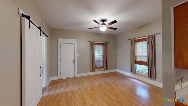 interior space featuring ceiling fan, a barn door, and light hardwood / wood-style flooring