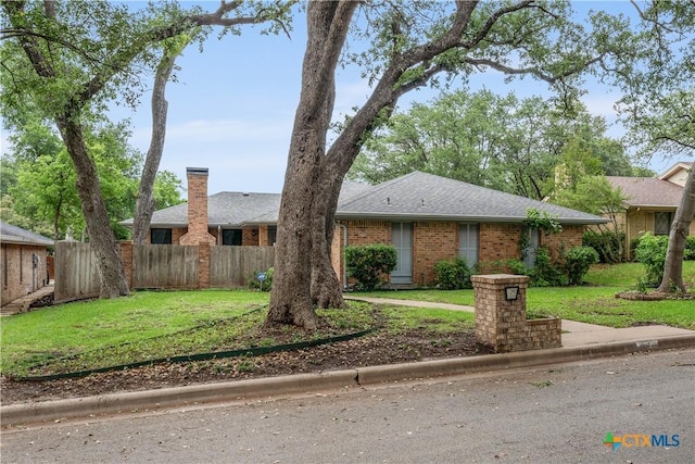ranch-style house with brick siding, fence, roof with shingles, and a front lawn