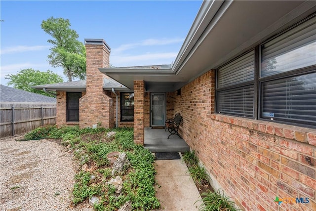 doorway to property featuring brick siding, fence, and a chimney