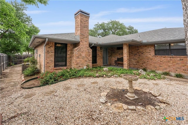 view of front facade featuring fence, a patio, roof with shingles, a chimney, and brick siding