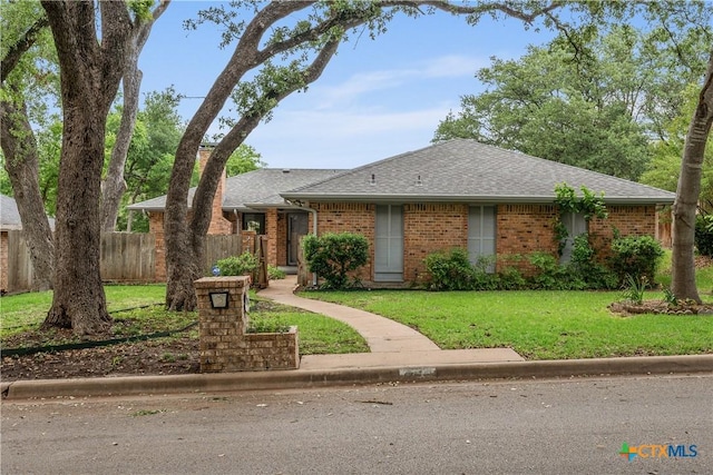single story home with a shingled roof, a front lawn, and brick siding