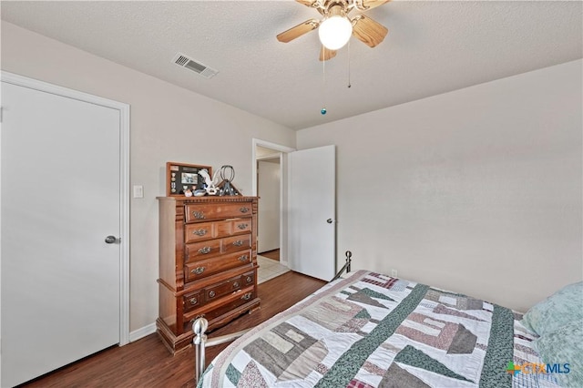 bedroom with a textured ceiling, a ceiling fan, wood finished floors, and visible vents