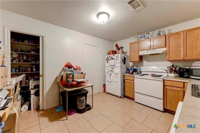 kitchen with a textured ceiling, light tile patterned flooring, and white appliances