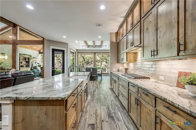 kitchen featuring beamed ceiling, light stone countertops, a spacious island, and light wood-type flooring