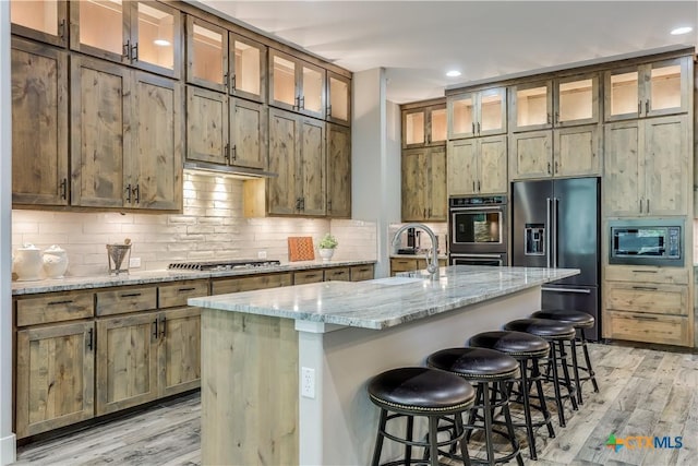 kitchen featuring light stone countertops, appliances with stainless steel finishes, light hardwood / wood-style flooring, a breakfast bar area, and an island with sink