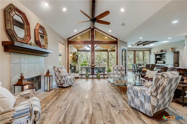 living room featuring vaulted ceiling with beams, light hardwood / wood-style floors, ceiling fan, and a tiled fireplace