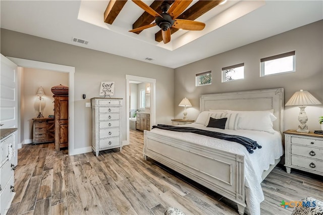 bedroom featuring a raised ceiling, ceiling fan, light hardwood / wood-style flooring, and ensuite bathroom