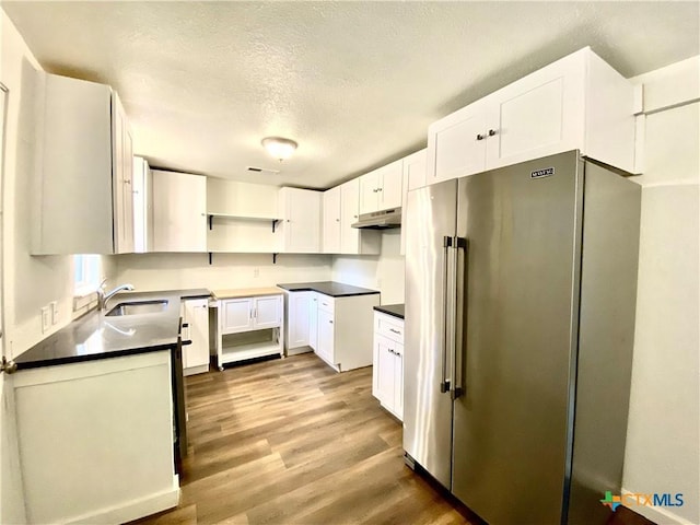 kitchen with white cabinets, sink, a textured ceiling, high quality fridge, and light hardwood / wood-style floors