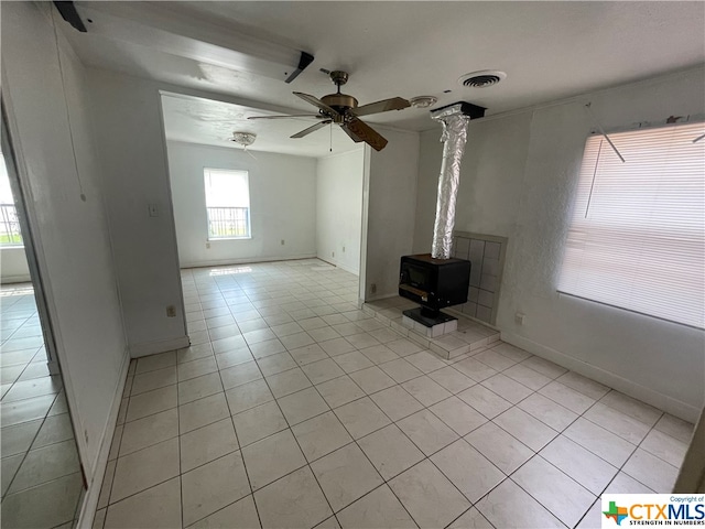 unfurnished living room featuring a wood stove, light tile patterned floors, and ceiling fan