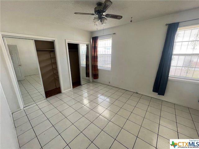 unfurnished bedroom featuring a textured ceiling, multiple closets, ceiling fan, and light tile patterned floors