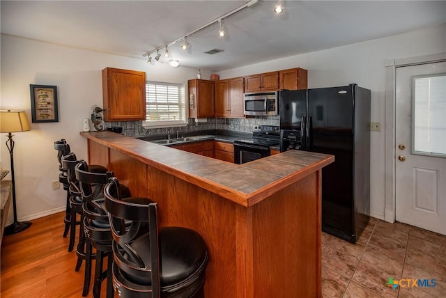 kitchen featuring sink, black appliances, a kitchen bar, decorative backsplash, and kitchen peninsula