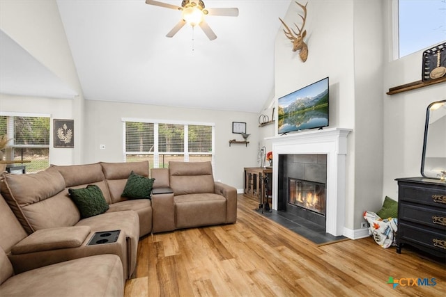 living area featuring a tiled fireplace, ceiling fan, wood finished floors, high vaulted ceiling, and baseboards