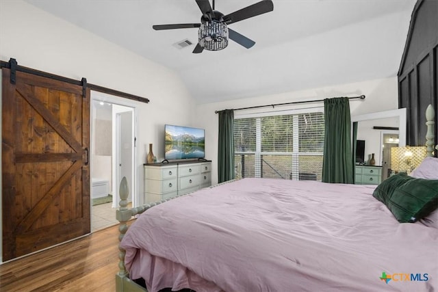 bedroom with a barn door, visible vents, a ceiling fan, wood finished floors, and vaulted ceiling