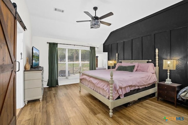 bedroom with vaulted ceiling, a barn door, light wood finished floors, and visible vents