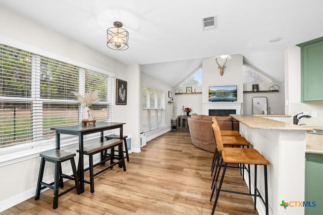 interior space featuring baseboards, visible vents, vaulted ceiling, light wood-type flooring, and a fireplace