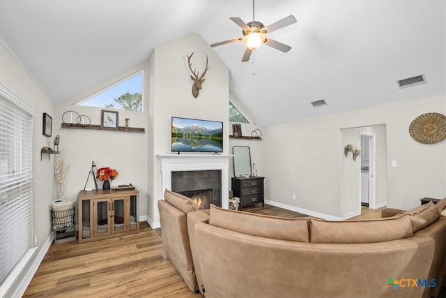 living area with a warm lit fireplace, light wood-style flooring, visible vents, and baseboards