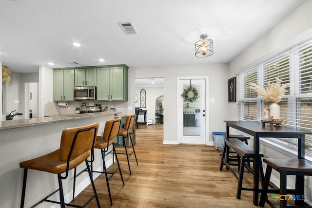 kitchen featuring a breakfast bar, visible vents, light wood-style floors, stainless steel microwave, and green cabinetry