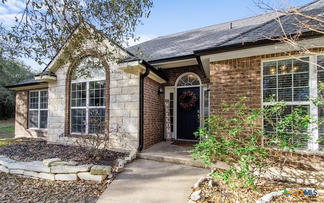 property entrance with a shingled roof and brick siding