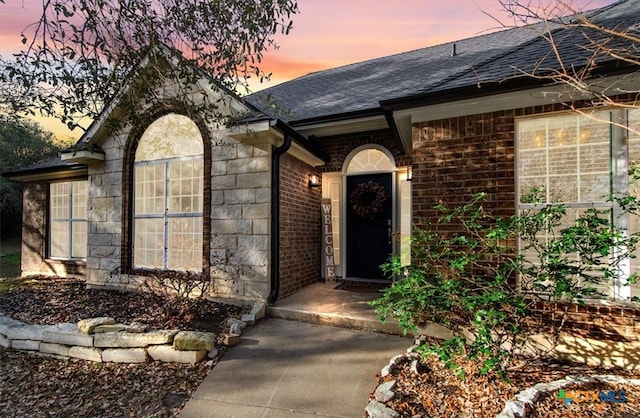 property entrance featuring stone siding, brick siding, and a shingled roof