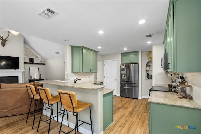 kitchen with stainless steel appliances, visible vents, light wood-style flooring, green cabinetry, and a peninsula