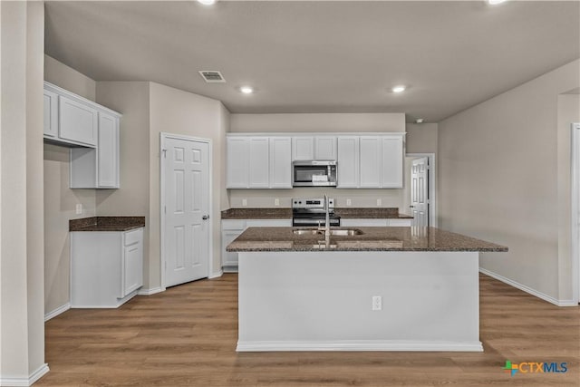 702 Stonevalley Rd, Temple, TX 76502 - kitchen featuring stainless steel microwave, white cabinetry, a kitchen island with sink, black range with electric cooktop, and wood finished floors