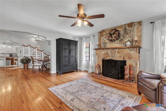 living room with a stone fireplace, hardwood / wood-style floors, and ceiling fan