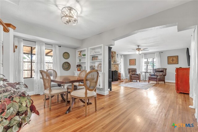 dining area with ceiling fan with notable chandelier, light hardwood / wood-style floors, and built in features