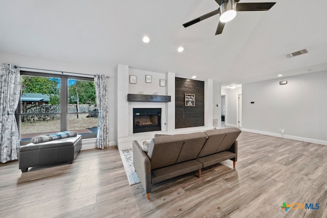 living room featuring a fireplace, ceiling fan, light hardwood / wood-style flooring, and lofted ceiling