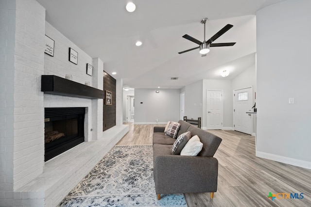 living room featuring ceiling fan, a large fireplace, light hardwood / wood-style floors, and lofted ceiling