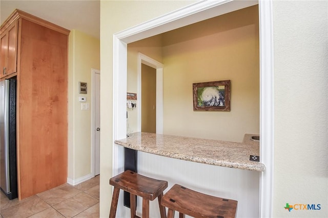1588 W Bayshore Dr, Palacios, TX 77465 - kitchen with freestanding refrigerator, a kitchen breakfast bar, light tile patterned flooring, and light stone counters