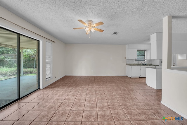 unfurnished living room featuring ceiling fan, a textured ceiling, light tile patterned floors, and sink