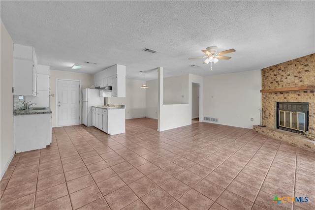 kitchen with white refrigerator, white cabinets, a textured ceiling, ceiling fan, and a fireplace