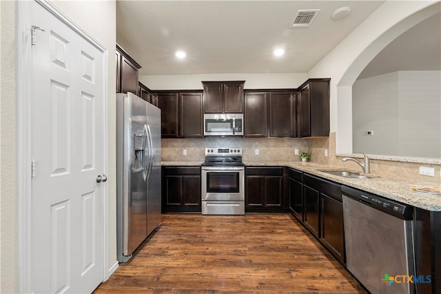1313 Juneberry Park Dr, Temple, TX 76502 - kitchen featuring stainless steel appliances, arched walkways, dark brown cabinets, a sink, and light stone countertops